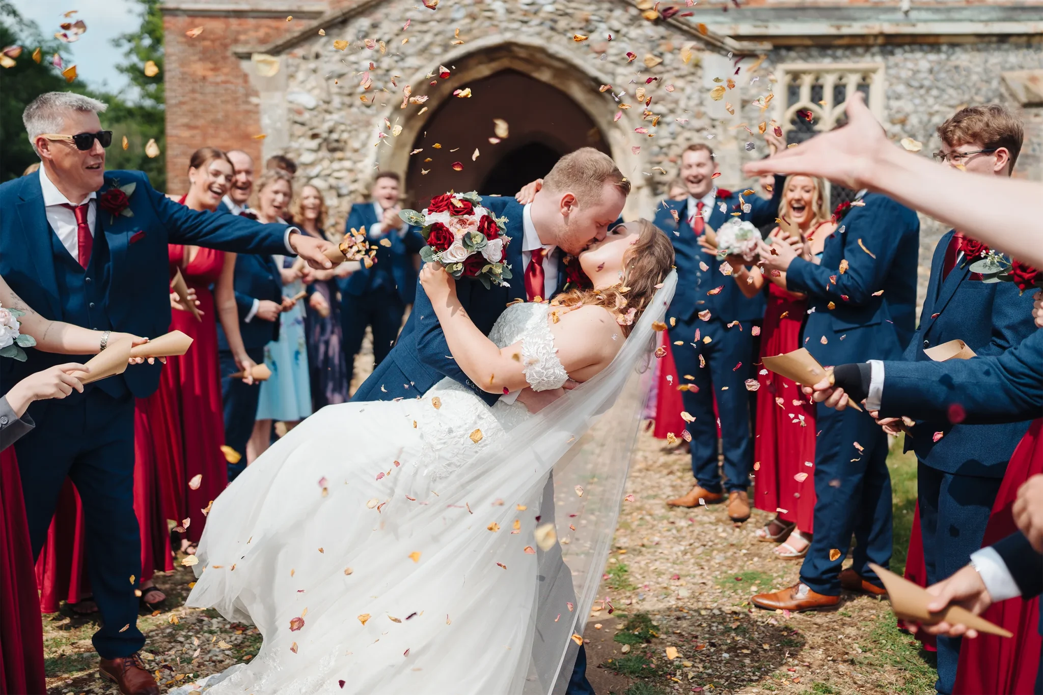 A couple sharing a kiss under a shower of confetti at a Norfolk wedding